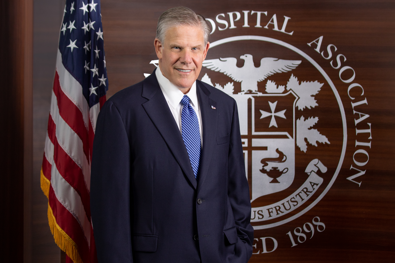 Rick Pollack standing in front of a flag with the American Hospital Association seal behind him.